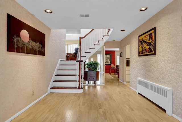 entrance foyer with visible vents, radiator heating unit, wood finished floors, baseboards, and stairs