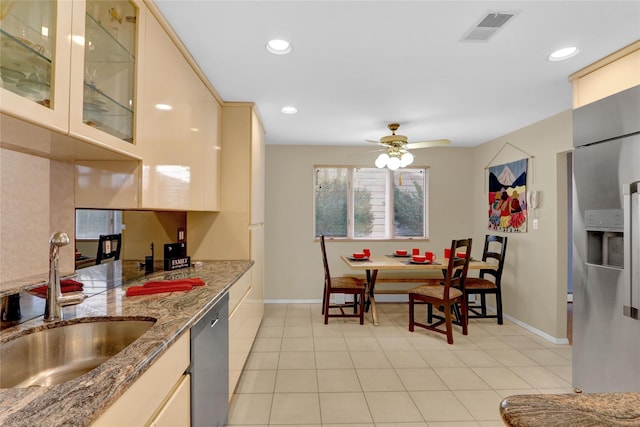 kitchen featuring stone counters, stainless steel appliances, a sink, visible vents, and glass insert cabinets