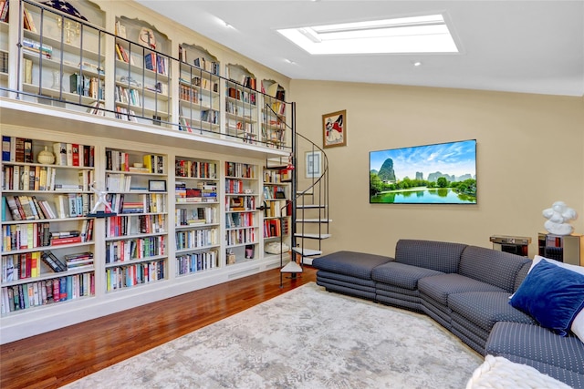 interior space featuring wall of books, lofted ceiling with skylight, and wood finished floors