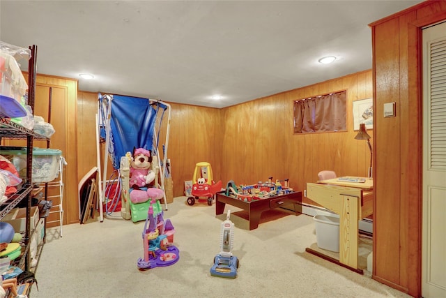 recreation room with a baseboard heating unit, wood walls, and light colored carpet