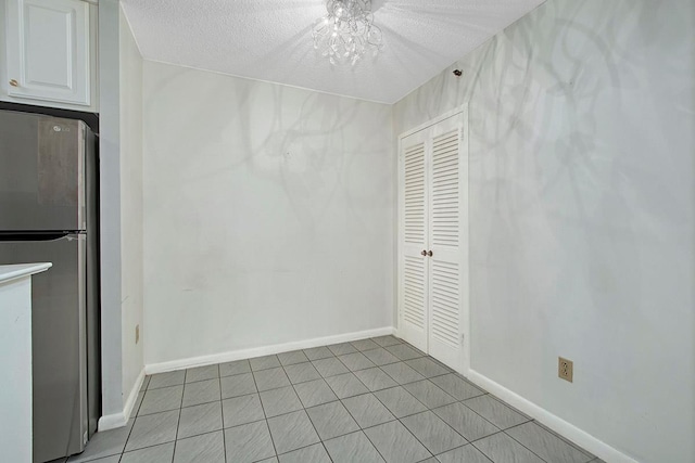 unfurnished dining area with a textured ceiling, light tile patterned floors, and baseboards