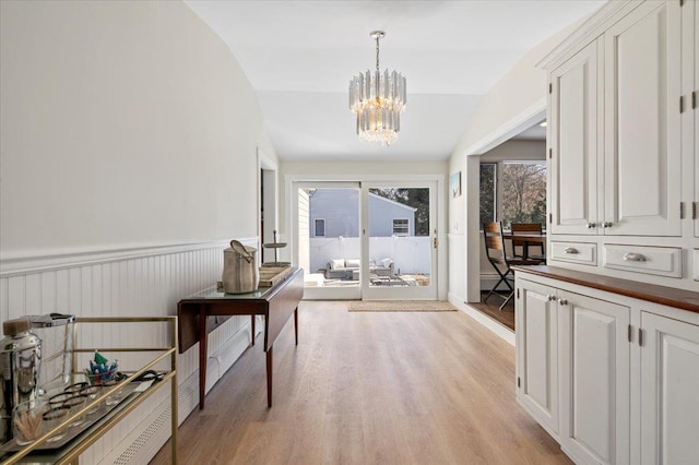 hall with lofted ceiling, a wainscoted wall, light wood-style flooring, and a notable chandelier