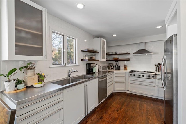 kitchen with dark wood-type flooring, a sink, appliances with stainless steel finishes, wall chimney exhaust hood, and tasteful backsplash