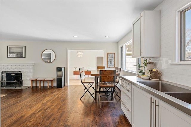 kitchen featuring dark wood-style flooring, a fireplace, decorative backsplash, white cabinetry, and a sink