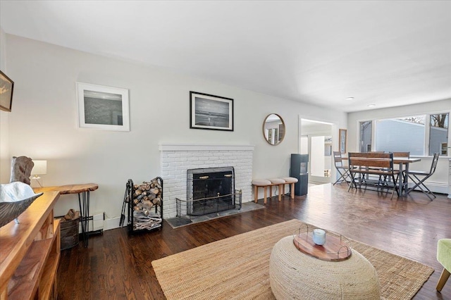 living room featuring a brick fireplace, baseboards, baseboard heating, and wood finished floors