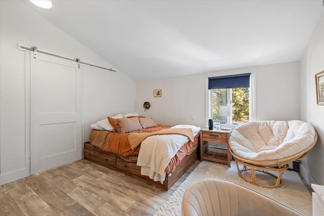 bedroom with lofted ceiling, light wood finished floors, and a barn door