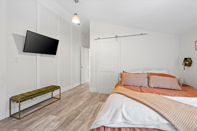 bedroom with lofted ceiling, a barn door, and light wood-style floors