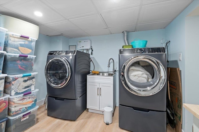 washroom featuring a sink, washing machine and dryer, cabinet space, and light wood-style floors