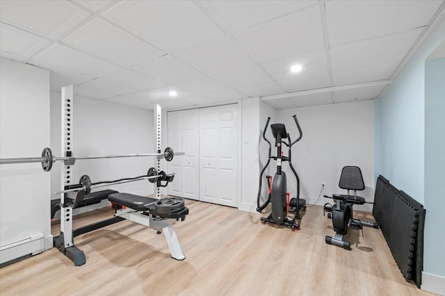 exercise area with a baseboard heating unit, a drop ceiling, wood finished floors, and baseboards