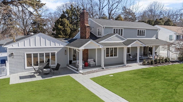 rear view of house featuring a chimney, a porch, a shingled roof, a lawn, and fence