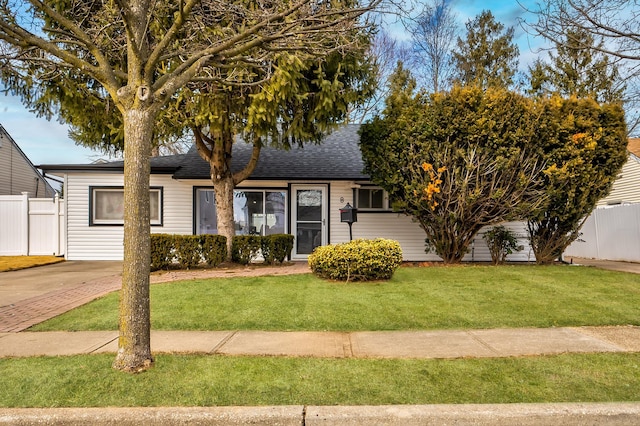 ranch-style house with a front yard, roof with shingles, and fence