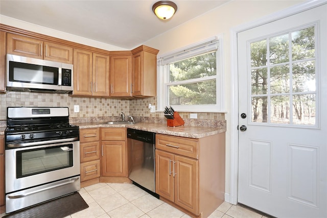 kitchen with light tile patterned floors, decorative backsplash, appliances with stainless steel finishes, brown cabinetry, and a sink