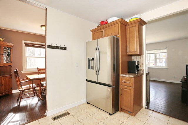 kitchen with visible vents, brown cabinetry, light countertops, stainless steel refrigerator with ice dispenser, and backsplash