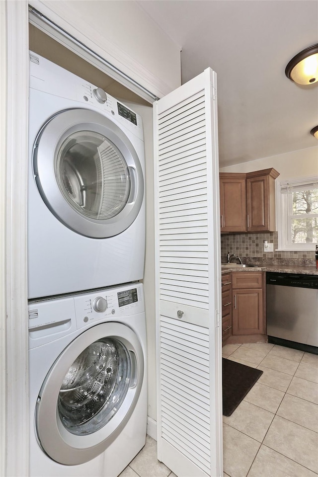 laundry area featuring stacked washer and clothes dryer, light tile patterned floors, a sink, and laundry area