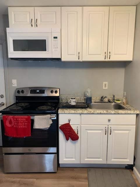 kitchen with white cabinets, white microwave, a sink, and stainless steel electric stove