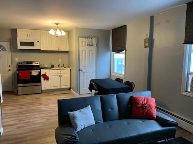 kitchen with white microwave, white cabinets, baseboard heating, light wood-type flooring, and stainless steel range with electric stovetop