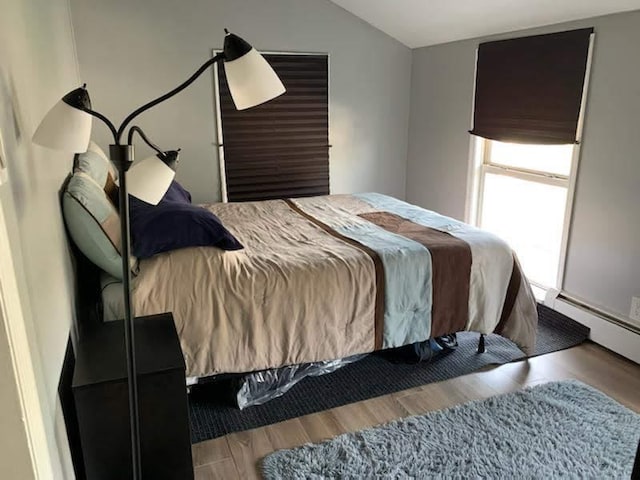 bedroom featuring a baseboard radiator, vaulted ceiling, and wood finished floors