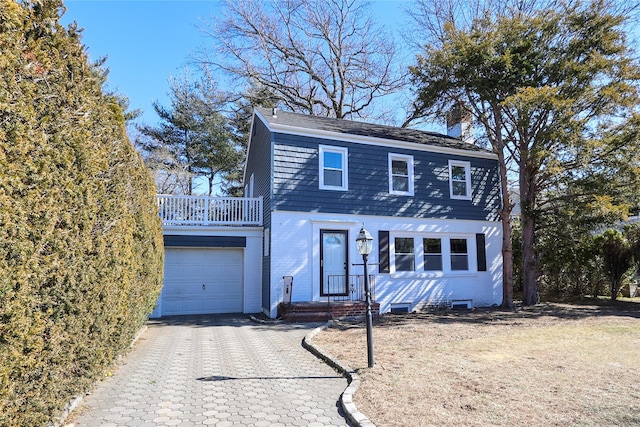 view of front facade with a garage, decorative driveway, brick siding, and a chimney