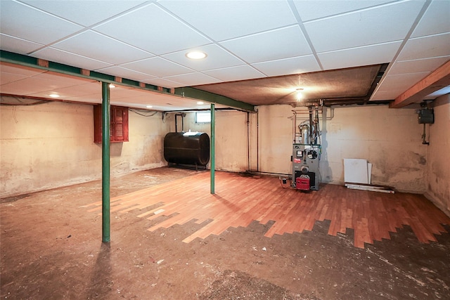 finished basement with a heating unit, wood finished floors, a paneled ceiling, and heating fuel