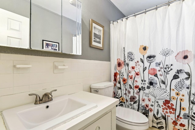 bathroom with a wainscoted wall, tile walls, a shower with shower curtain, toilet, and vanity