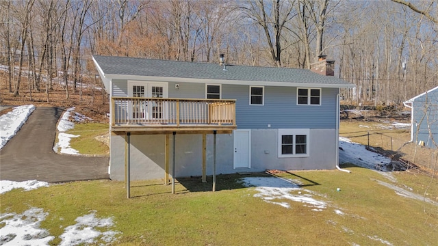 rear view of property featuring a chimney, a wooden deck, and a lawn