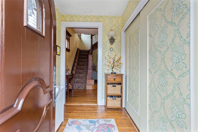 corridor featuring wallpapered walls, stairway, and light wood-style floors