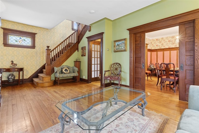 living room featuring wallpapered walls, stairs, baseboards, and light wood finished floors