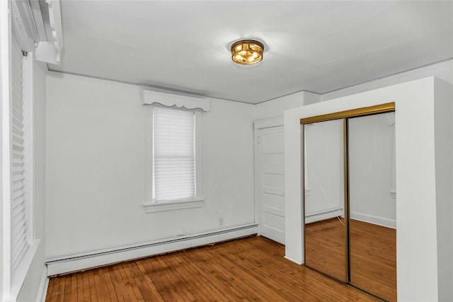 unfurnished bedroom with hardwood / wood-style flooring, a baseboard heating unit, and a closet