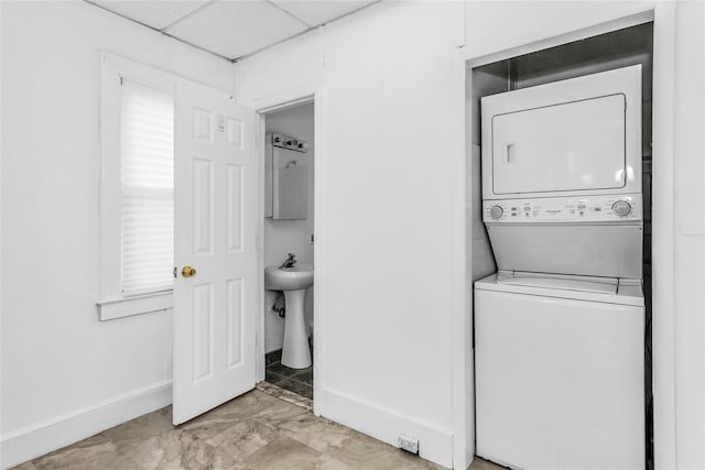 laundry area with marble finish floor, stacked washer and dryer, a sink, laundry area, and baseboards