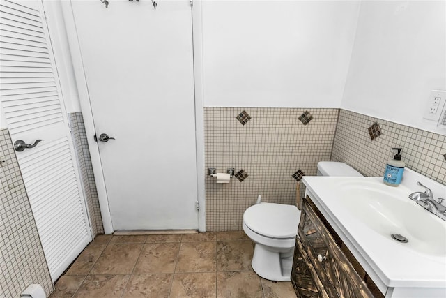 half bathroom with tile walls, wainscoting, vanity, and toilet