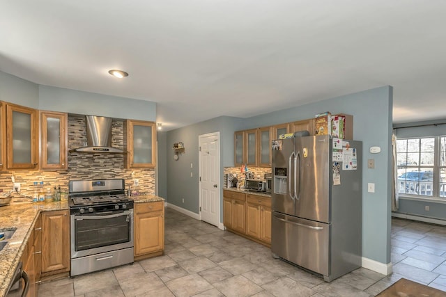 kitchen with appliances with stainless steel finishes, baseboard heating, light stone countertops, wall chimney exhaust hood, and glass insert cabinets