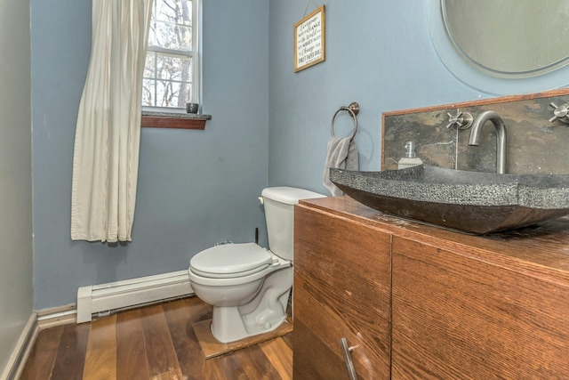 half bath featuring toilet, baseboard heating, vanity, wood finished floors, and baseboards