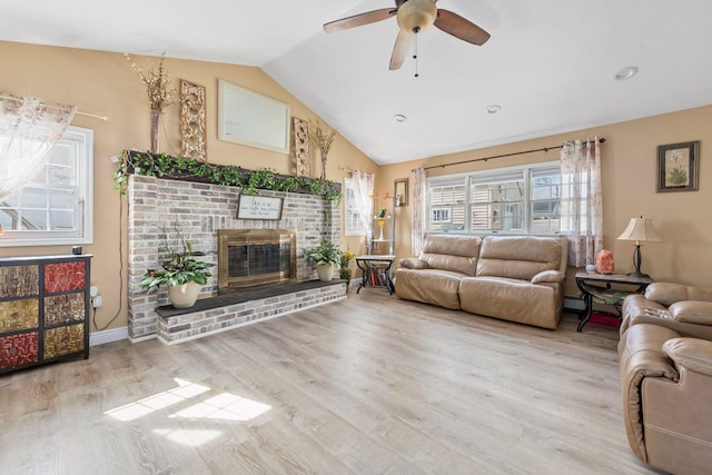 living room with baseboards, ceiling fan, vaulted ceiling, light wood-type flooring, and a brick fireplace