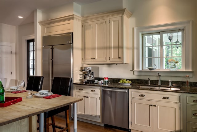 kitchen featuring appliances with stainless steel finishes, dark stone counters, a sink, and recessed lighting