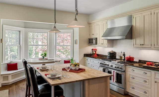 kitchen featuring butcher block counters, a kitchen island, appliances with stainless steel finishes, wall chimney exhaust hood, and pendant lighting