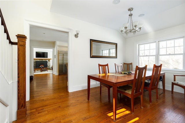 dining space featuring baseboards, lofted ceiling, dark wood-style floors, a stone fireplace, and a chandelier