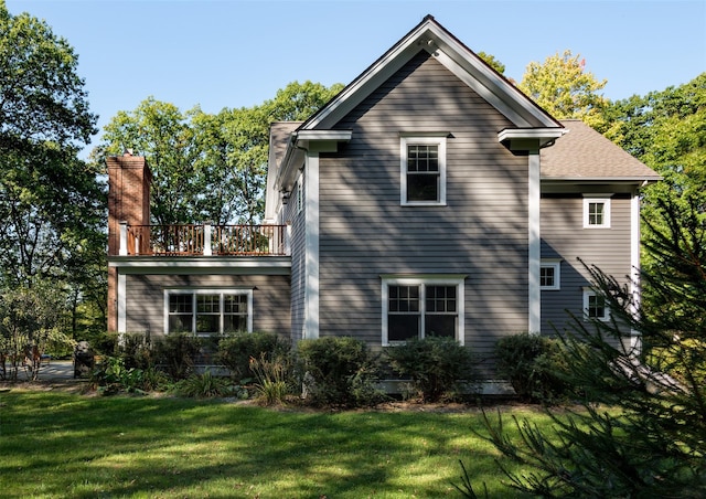 back of property with a balcony, a chimney, and a lawn