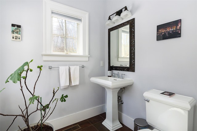 half bathroom with baseboards, visible vents, toilet, tile patterned flooring, and a sink