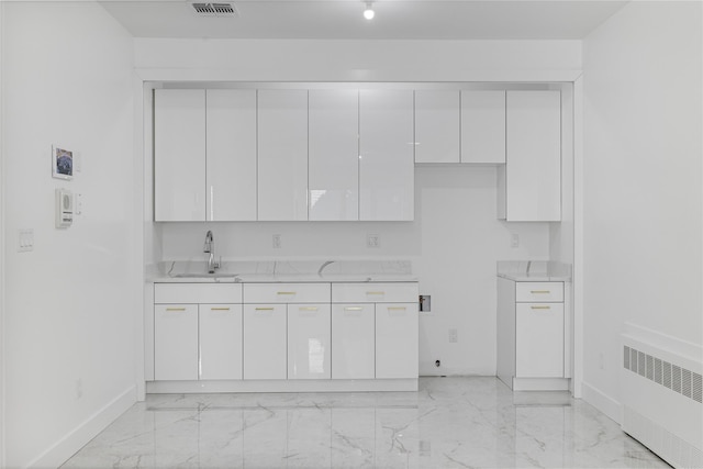 kitchen with marble finish floor, radiator, light countertops, white cabinets, and a sink