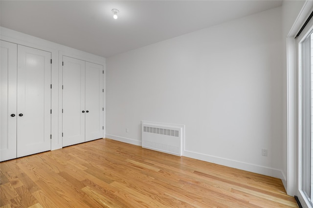 unfurnished bedroom featuring light wood-type flooring, radiator, baseboards, and two closets