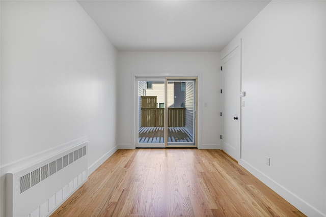 unfurnished room featuring radiator heating unit, light wood-type flooring, and baseboards