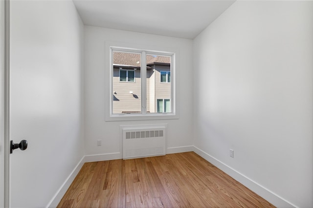 spare room featuring baseboards, radiator heating unit, and light wood-style floors