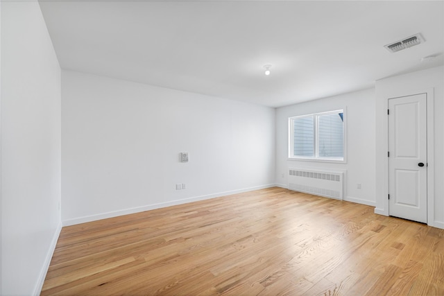 empty room with baseboards, light wood-style flooring, visible vents, and radiator