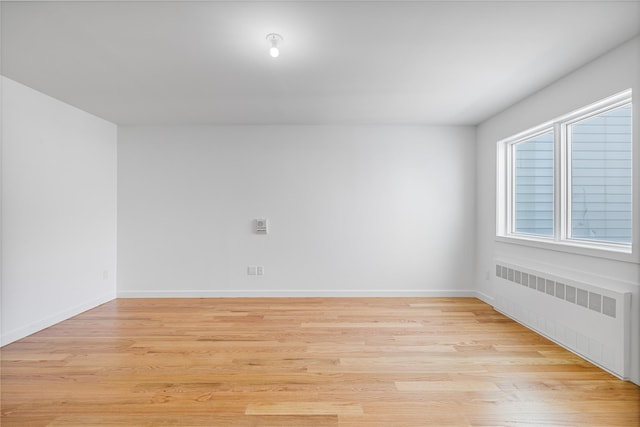 spare room with radiator, baseboards, and light wood finished floors