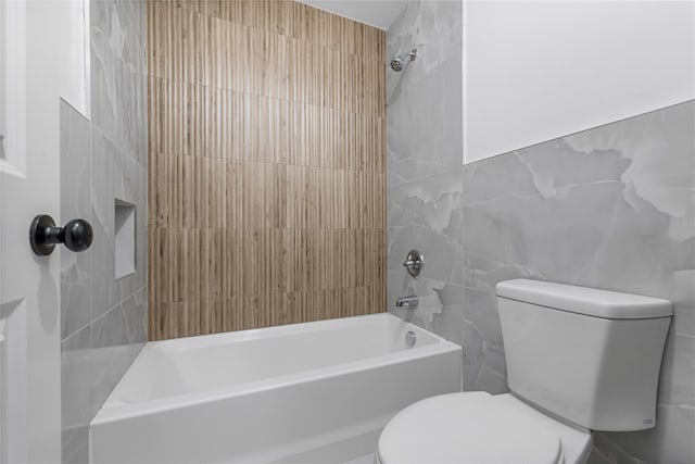 bathroom with toilet, shower / washtub combination, and tile walls