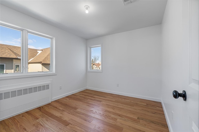 spare room featuring baseboards, wood finished floors, and radiator