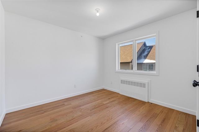 empty room with baseboards, light wood finished floors, and radiator heating unit