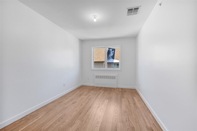 empty room featuring radiator, light wood finished floors, baseboards, and visible vents