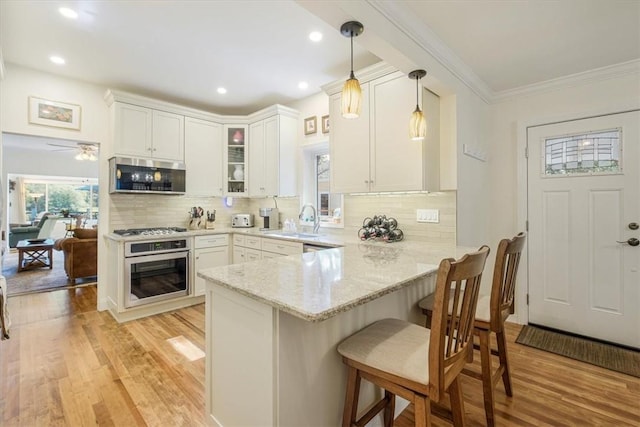 kitchen featuring a breakfast bar area, light stone countertops, a peninsula, a sink, and appliances with stainless steel finishes