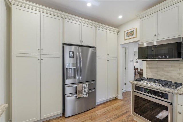 kitchen featuring light wood finished floors, recessed lighting, decorative backsplash, white cabinets, and appliances with stainless steel finishes